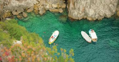 Capri, İtalya 'da kayalık körfez yakınlarında açık yeşil suda yüzen üç tekne..