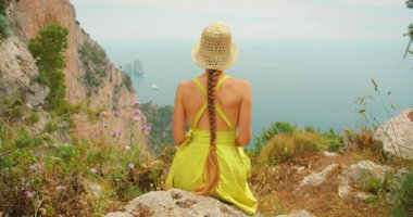 Faraglioni 'ye tepeden bakan uçurumun kenarında oturan kadın puslu bir günde Capri' deki kayaları sarıyor..