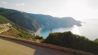 Kefalonya 'daki kayalıklarla çevrili geniş bir yaz koyuna bakan kadın ayakta duruyor.