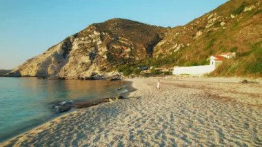 Yazın altın saatinde Kefalonia 'daki Petani Plajı' nda tek başına yürüyen bir kadın..