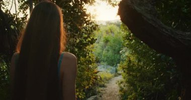 Mangrov ağaçları arasında dar bir orman patikasında ışığa doğru yürüyen kadının arka görüntüsü..