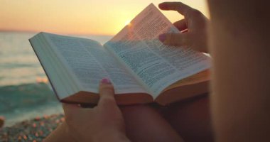 Hırvatistan 'da yaz günbatımında çakıllı bir plajda kitap okuyan kişi.