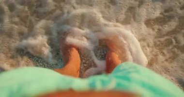 Sığ deniz suyunda gün batımında ayaklarına dokunan dalgalarla duran kişi.