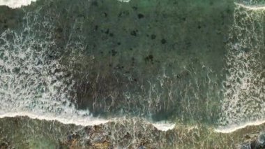 Yeşil denizdeki sığ kayalık kayalıkların üzerinde köpüklü dalgaların üst hava manzarası.