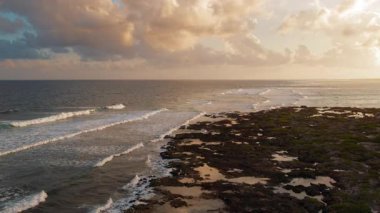 Dalgalar, altın saat günbatımında kıyı şeridi boyunca volkanik kayaları yıkıyor..