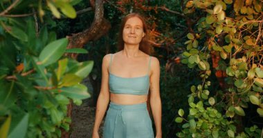 Gün batımında yemyeşil bir tropikal ormanda huzur içinde yürüyen bir kadın..