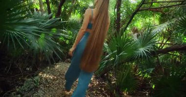 Son derece uzun saçlı bir kadın yeşilliklerle çevrili orman yolunda yürüyor..