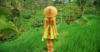 Bali pirinç terasında uzun otların üzerinde hasır şapka takan bir kadın..