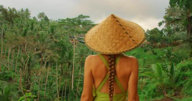 Pirinç tarlası gezisi sırasında Bali orman manzarasına hayran olan koni şapkalı kadın..