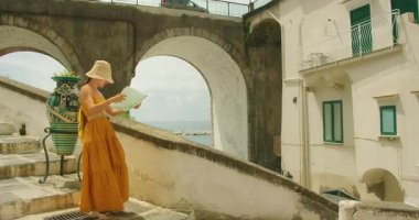 Yaz aylarında büyük vazo ve taş kemerli köprünün yanındaki sahil merdivenlerinde yürüyen ve harita okuyan bir kadın..