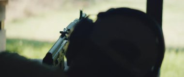 Bir insan, açık hava atış poligonunda bir bipoda tüfeği ateşlemeye hazırlanıyor..