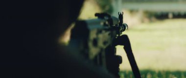 Tetikçi arka planda hedef menzili ile tüfekle nişan alıyor..