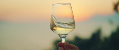 Renkli günbatımına karşı tutulan şarap kadehi yaz akşamları gökyüzü ve deniz manzarası.
