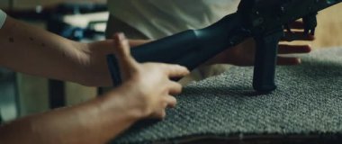 Eğitmen, ateşli silah güvenliği eğitimi sırasında tüfek tutan kadına rehberlik eder..