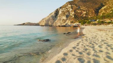 Kefalonya 'da sakin bir sahil boyunca, dalgalar ve tepelerle yürüyen bir kadın..