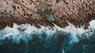 Deniz dalgalarının buluştuğu hava görüntüsü gün batımında kayalık kıyı şeridini deldi..