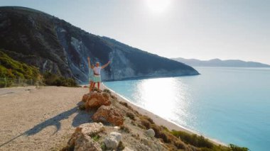 Çift, Kefalonia 'da mavi suları olan sakin bir Myrtos plajının üstündeki kayalıklarda poz veriyor..