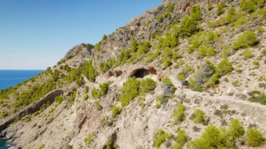 Mağara yakınlarındaki kayalık dağ patikalarında yürüyen bir kadın ve Kefalonia kıyı şeridinde çam ağaçları.