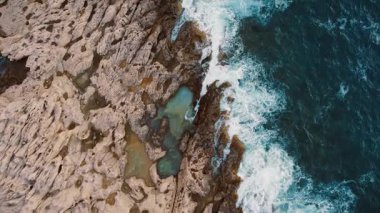 Kıyı kaya platformlarının etrafında, havadan bakıldığında dalgalar ve dalgalar dolaşır..