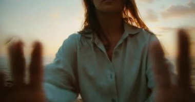 Sahilde gün batımında kamerayı iten dansçı kadının yakın çekimi.