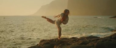 Gün batımında deniz kenarındaki kayalarda çağdaş dans eden bir kadın..