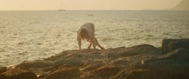 Dansçı kadın, alacakaranlıktaki deniz kenarı gösterisinde zarifçe eğiliyor..