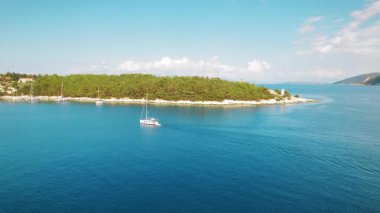 Fiskardo köyü yakınlarındaki deniz feneri ve ormanın yanından geçen yat..