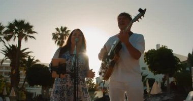 Şarkıcılar altın saat boyunca arkada palmiye ağaçları ve binalarla gösteri yapıyorlar..