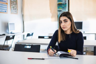 Genç ve güzel bir kadın gazetelerle masada otururken yazı yazıyor.