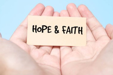 Elinde kağıt tutan kadın mavi arkaplanlı Umut ve İnanç kelimelerini heceliyor. Kadının avuçlarında 