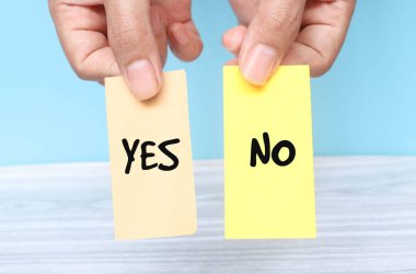 Woman holding two yellow and brown paper spelling words Yes or No on blue background. Torn piece of paper with the words 