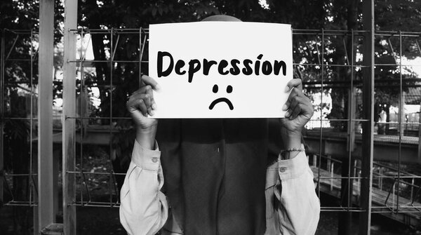 Woman holding paper covering her face with depression message and sad emoji on black and white background. Motivational words about life