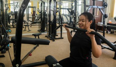 Genç kız spor salonunda Lat Pulldown Machine üzerinde çalışıyor. Kol ve göğüs kası eğitiminde.