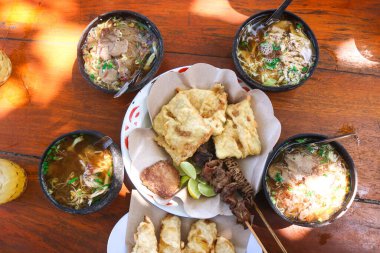 Soto Ayam ve et soto hindistan cevizi kabuğu kabukları içinde ahşap masa üzerinde mendoan aperatifleri, satay ve içecekler. Geleneksel Endonezya çorbası temel olarak et, tavuk ve sebzelerden oluşur..