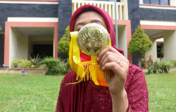 Mezuniyet madalyasını kameraya gösteriyor. Yogyakarta Devlet Üniversitesi 'nde mezuniyet günü kutlaması.