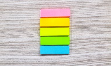 Tahta masadaki kitaplar için beş renkli yer imi. Gri arkaplandaki renkli kağıt notlar veya yer imleri. Günlük ve ofis masası kavramı