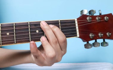 G temel anahtarlar gitar dersi serisi. Gitarda G majör akorunu çalan elin yakın plan görüntüsü mavi arkaplanda izole edilmiş.