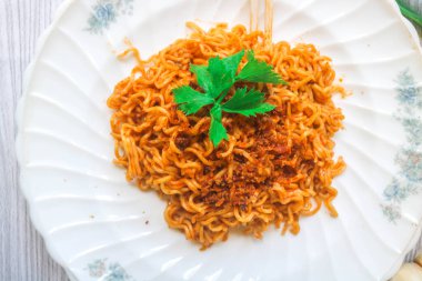 Tahta bir masada, üzerinde kızarmış soğan ve sebzeler olan baharatlı hazır şehriye manzarası. Fast food eriştesinin baharatlı bir çeşidi.