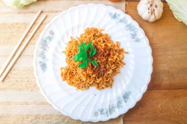 Tahta bir masada, üzerinde kızarmış soğan ve sebzeler olan baharatlı hazır şehriye manzarası. Fast food eriştesinin baharatlı bir çeşidi.