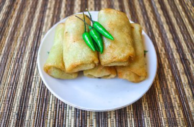 Lumpia or fried spring rolls are a food made from flour filled with vegetables such as carrots, cabbage, sprouts and eggs. Lumpia or fried spring rolls on a white plate served with chili clipart