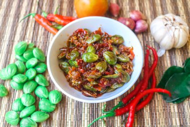 Sambal Pete or petai with small shrimps served in a white bowl on the table with other condiments. Sambal or popular Indonesian sauce. clipart