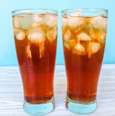 Masadaki mavi arka planda izole edilmiş büyük bardakta buzlu çay. Taze buzlu çay.