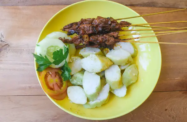 Tipik Endonezya yemeği tavuk satayını (tavuk satay) fıstık sosu ve ahşap bir masada servis edilen lontong pirinci ile kapatın. Endonezya mutfağı et satay kavramı