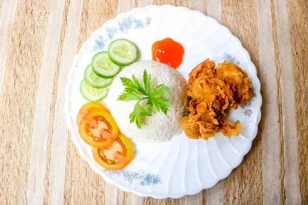 Baharatlı soslu kızarmış tavuk ve salatalık, domates ve kereviz gibi sebzelerle garnitür olarak servis edilir. Ahşap masada kızarmış tavuk ve pilav.