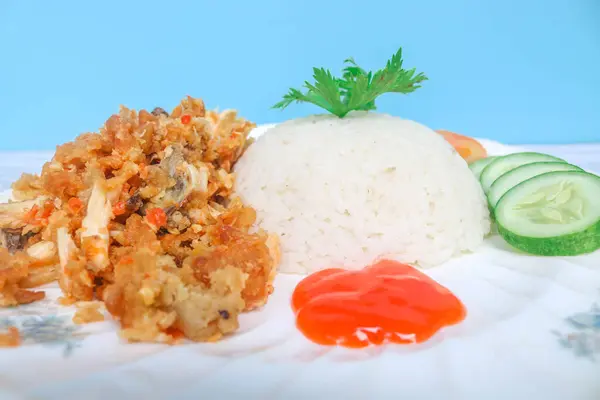 stock image Ayam Geprek or Fried chicken with sauce chili sambal served with rice and vegetable like cucumber, tomato and celery as garnish. Indonesia popular food Ayam Geprek hot chili served on wooden table