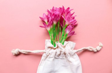 Top view photo of bouquet of pink lilies in a string bag isolated pink background with copyspace. Spring flowers on pink flat lay. Greeting card, holidays concept. Zephyranthes grandiflora flower clipart