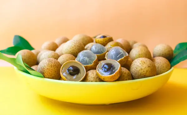 Sarı arka planda yaprakları olan taze yerel longan meyveleri, Asya tropikal meyveleri. Bahçedeki Longan hasadı