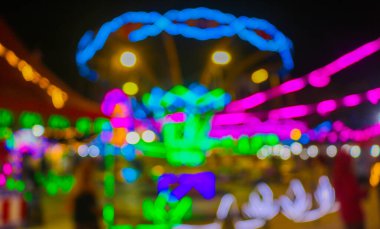 Gece festivalinde Bokeh arka planlı bir lunaparktaki atlı karınca turunun bulanık görüntüsü. Gece festival parkındaki eğlenceli gezintilerin gece renkli ışıklarla çekilmiş soyut bulanık fotoğrafı..