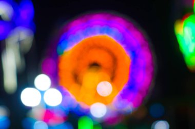 Gece festivalinde Bokeh arka planlı dönme dolabın bulanık görüntüsü. Gece festival şehir parkındaki oyun sürüşlerinin soyut bulanık fotoğrafı gece renkli ışıklarla bokeh arka plan.