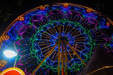Gecenin karanlığında dönme dolap renkli ışığa çok yakın. Gece pazarı festivalinde dönme dolap, lunapark gezileri